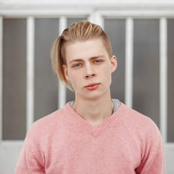 Retrato de um jovem bonito com um corte de cabelo em uma camisola rosa — Fotografia de Stock