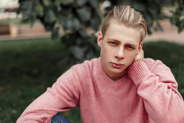 Elegante joven guapo en suéter rosa se sienta en el parque — Foto de Stock