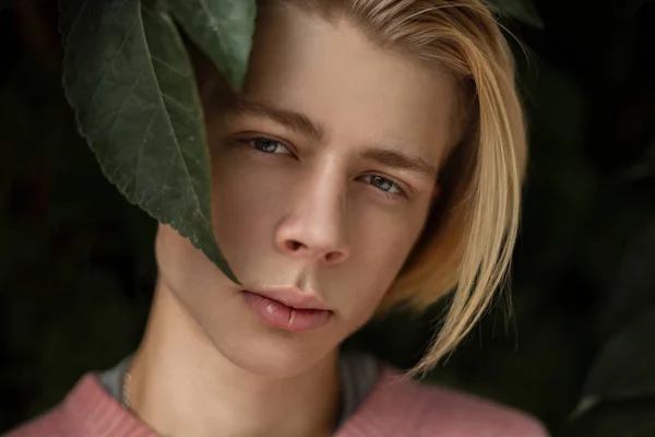 Retrato natural de um jovem bonito com um penteado loiro na folhagem — Fotografia de Stock