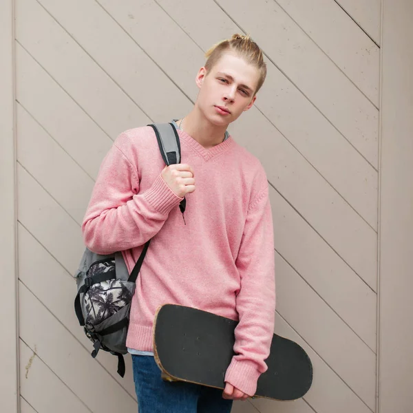 Yakışıklı genç model Pembe moda kazaklı bir sırt çantası ve kaykay ile bir saç modeli ile