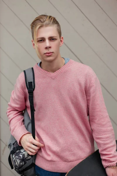 Yakışıklı genç bir sırt çantası ve plaja yakın bir ahşap duvar kaykay ile