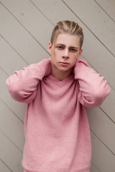Joven guapo con el pelo rubio en un suéter rosa de moda cerca de una pared de madera —  Fotos de Stock