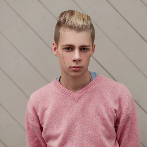 Yakışıklı genç bir pembe kazaklı bir ahşap duvar yakınındaki bir saç modeli ile