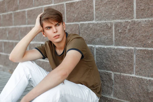 Bir tuğla duvara yakın oturan bir klasik T-shirt yakışıklı genç adam