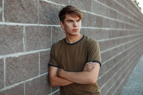 Handsome young guy in a classic T-shirt near a brick wall on the street