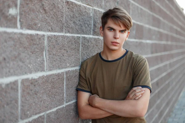 Porträtt av en ung stilig man i en klassisk T-shirt står nära en tegelvägg — Stockfoto