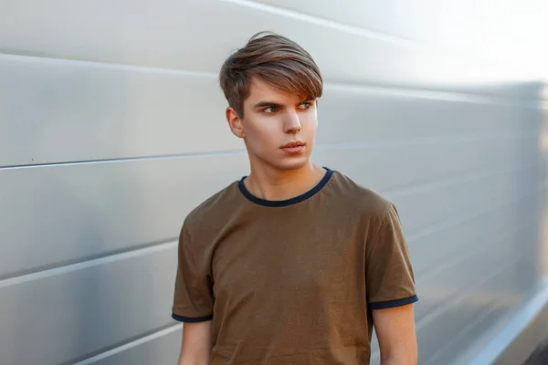 Moderna porträtt av en ung man med en frisyr i en klassisk T-shirt på en grå bakgrund — Stockfoto