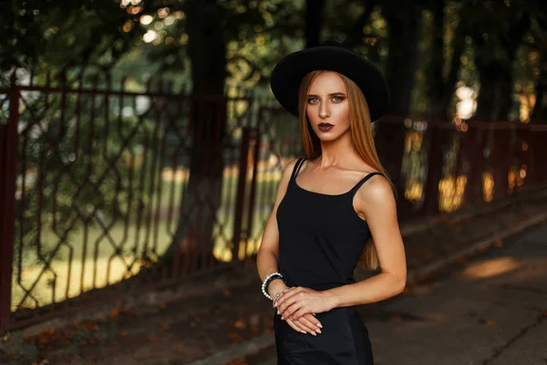 Hermosa joven en ropa de moda negra con sombrero en el parque —  Fotos de Stock