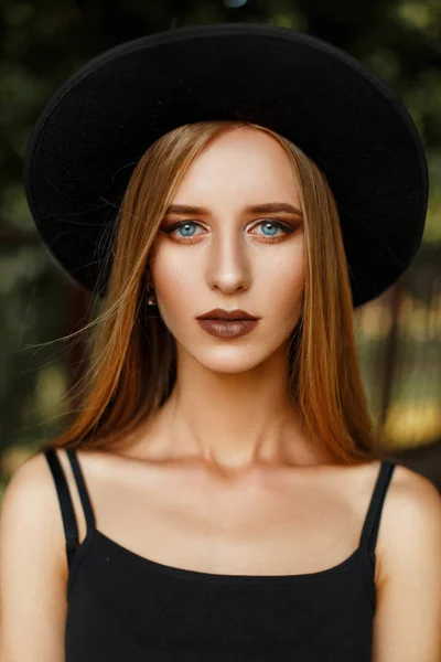 Fashion portrait of a beautiful woman with makeup with blue eyes in a black stylish hat outdoors — Stock Photo, Image