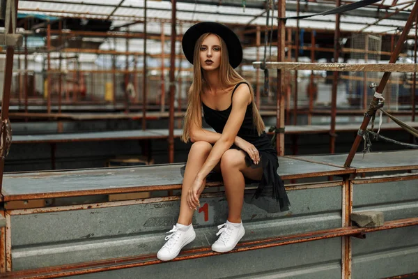 Güzel genç kadın trendy siyah şapka ve boş bir pazarda oturan beyaz ayakkabılarla etek