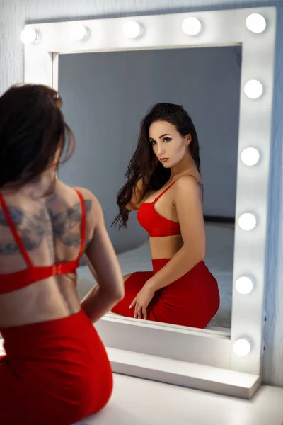 Menina bonita em roupa interior sexy vermelha senta-se perto de um espelho vintage com lâmpadas — Fotografia de Stock