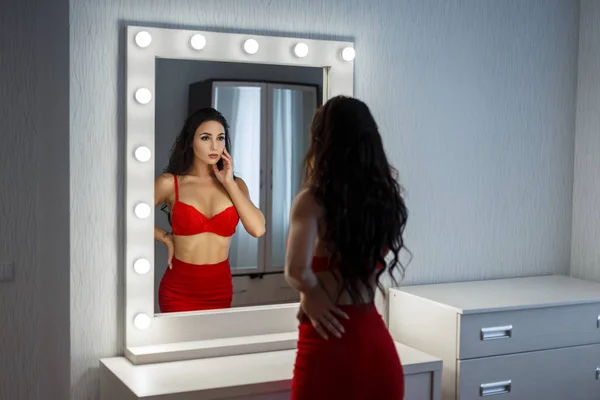 Vacker ung kvinna med en sexig kropp i rött underkläder och en röd kjol ser ut i en vintage spegel — Stockfoto