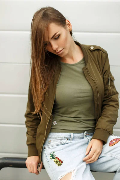 Schöne junge Frau mit Sommersprossen im Straßenstil in einer Jacke und einem T-Shirt mit Jeans in der Nähe einer Metallwand — Stockfoto
