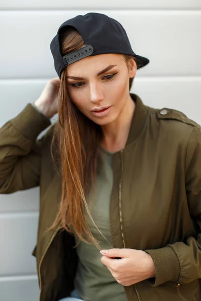 Πορτρέτο του μια όμορφη νεαρή γυναίκα σε ένα μαύρο μπέιζ-μπώλ ΚΑΠ σε μια μοντέρνα μπουφάν που κοιτάζει προς τα κάτω — Φωτογραφία Αρχείου