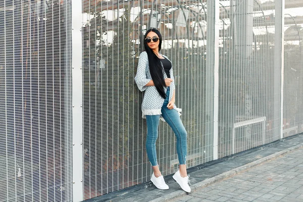 Uzun saç moda iyi giysiler ve duvarın yanında beyaz spor ayakkabı ile şık güzel model kız