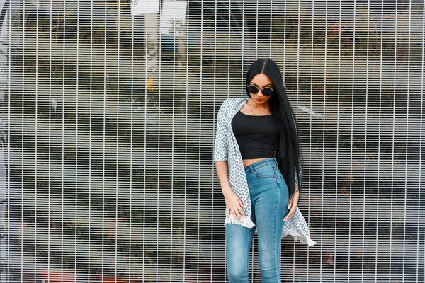 Duvara yakın poz trendy rahat kot giyim güneş gözlüğü ile uzun bakımlı saçları güzel genç kız