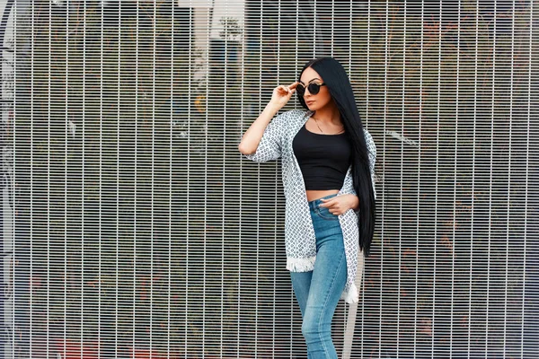 Belle femme hipster à la mode portant des lunettes de soleil vintage rondes dans des vêtements à la mode près du mur — Photo