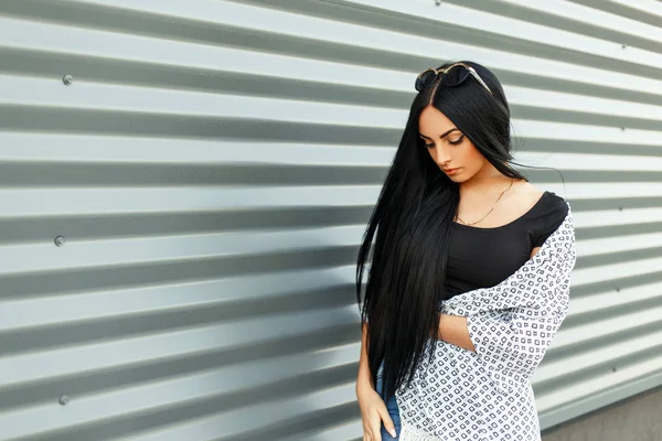 Bela morena com cabelos longos em roupas da moda perto de uma parede de metal na rua — Fotografia de Stock