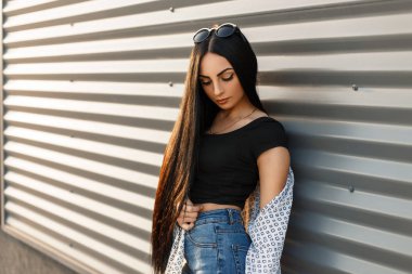 Güneşli bir günde bir metal duvar yakınındaki trendy kıyafetler içinde su kuyusu-damat saçlı güzel genç kadın