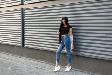 Moda model kadın şık yaz giysileri beyaz ayakkabılarla modern bir duvara yakın poz