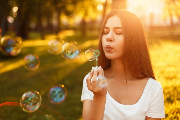 Hermosa joven que sopla burbujas de jabón en el parque al atardecer — Foto de Stock