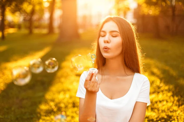 Feliz joven hermosa mujer con burbujas de jabón descansando en el parque al atardecer — Foto de Stock