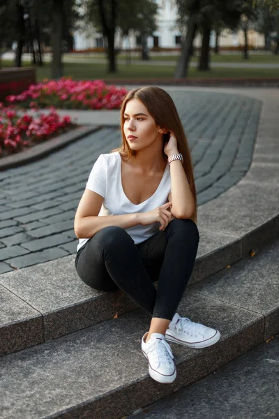 Belle jeune fille dans un T-shirt blanc jeans noirs en baskets blanches se trouve dans le parc — Photo
