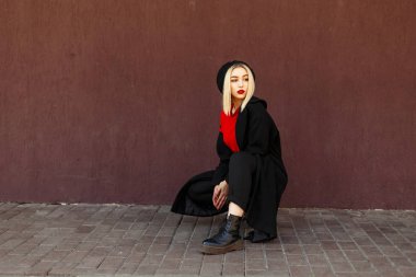 Güzel genç kadın sokakta bir duvarının yakınında oturan sonbahar moda giysileri