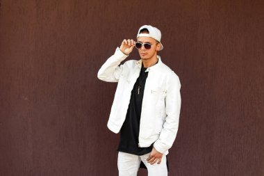 Beysbol şapkası duvara yakın poz güneş gözlüğü ile beyaz şık ceket şık yakışıklı adam