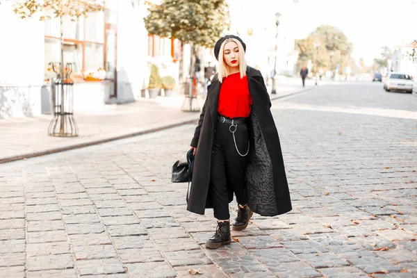 Mulher bonita na moda em um casaco na moda preto com uma boina com uma bolsa de mão em sapatos andando na cidade — Fotografia de Stock