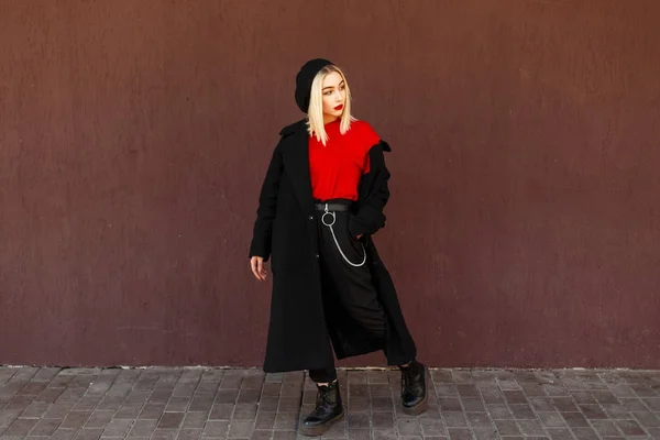 Mujer joven y elegante en un abrigo negro de otoño con una boina y botas cerca de la pared — Foto de Stock