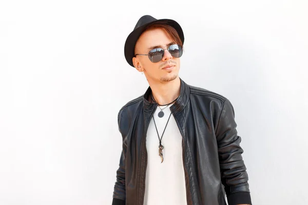 Stylish handsome young man in a black hat with sunglasses in fashion black jacket posing on white background — Stock Photo, Image