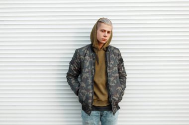 Yakışıklı genç trendy askeri ceket beyaz metal yakınındaki bir kukuleta ile kör