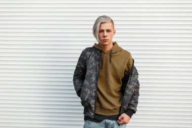 Beyaz metal duvara yakın poz hoodie trendy askeri ceketle şık yakışıklı adam