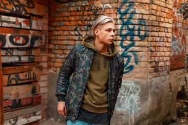 Yakışıklı erkek manken duvarının yakınında askeri ceketli 