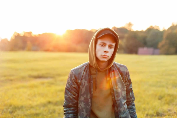 Handsome man in a stylish military jacket with hood in nature at sunset — Stock Photo, Image