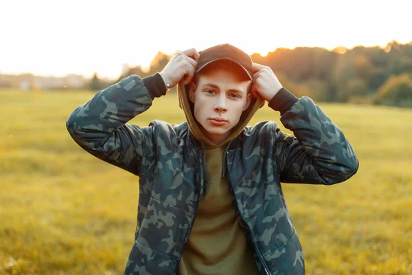 Csinos, fiatal férfi-egy katonai kabát egy kalap és egy pulóver, napnyugtakor a természet — Stock Fotó