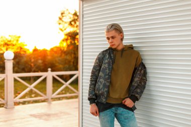 Yakışıklı genç bir askeri ceket ve gün batımında sahilde şık kapüşonlu