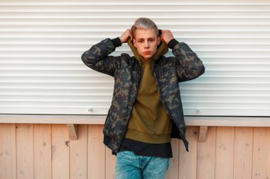 Şık yakışıklı askeri ceket ve beyaz metal walls yakınındaki hood koyar