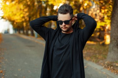 güneş gözlüğü ve bir siyah kazak şık yakışıklı kaputun üzerine güneşli bir sonbahar gününde koyar.