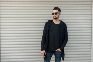 Şık yakışıklı siyah hoody metal duvara yakın poz içinde güneş gözlüğü