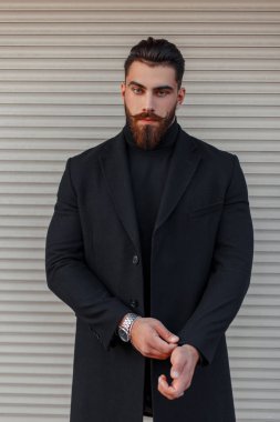 Şık genç bir saç modeli ile adam ve metal bir duvara yakın poz trendy siyah paltolu sakal