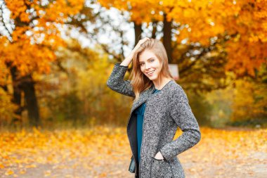 Bir sonbahar günü şık moda giysileri sarı yapraklar yakınındaki bir gülümseme ile mutlu kadın