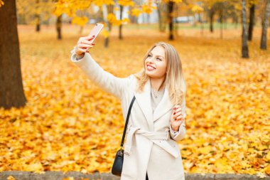 Sarı sonbahar yaprakları bir arka plan üzerinde bir resim çekmek bir telefon olan mutlu kadın