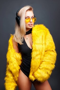Sarı güneş gözlüğü ve gri bir arka planda müzik dinlemek sarı kürk manto şık güzel genç kadın. DJ kız stüdyoda
