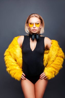 Vogue şık güzel genç Dj kız kulaklık güneş gözlüğü ile sarı gözlük ve moda sarı kürk ceket gri bir arka plan üzerinde