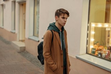 Genç model adam sokakta vitrin yakınındaki bir moda çanta vintage moda paltolu bir saç kesimi ile