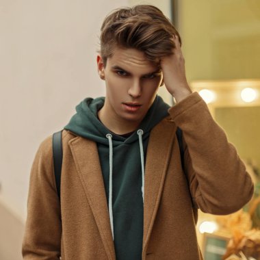 Vitrinler yakınında sokakta vintage paltolu bir saç kesimi ile yakışıklı genç bir adam portresi