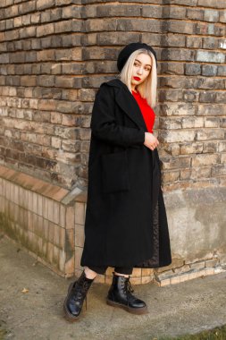 Kırmızı Jersey'de bir vintage tuğla duvar yakınındaki bir siyah bere ile siyah paltolu güzel şık kadın