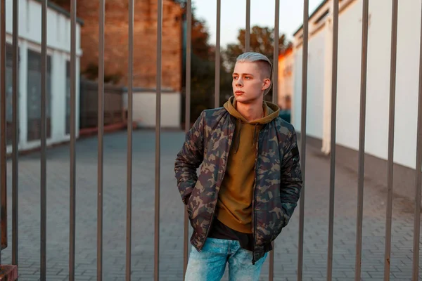 Elegáns csinos, fiatal férfi-egy trendi katonai kabát, farmer, közel a kerítés — Stock Fotó